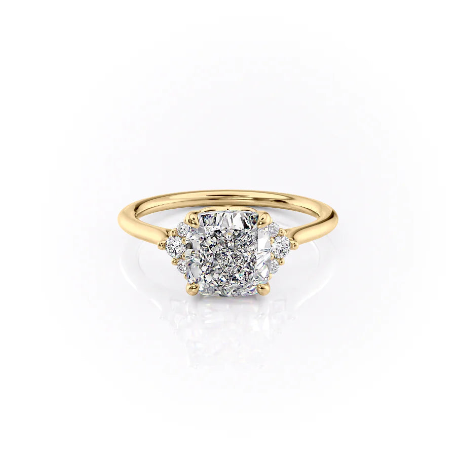 The Victoria. A Yellow Gold Three Stone, Side Stones Engagement Ring Set With A 2ct Cushion Lab Grown Diamond. White Background.