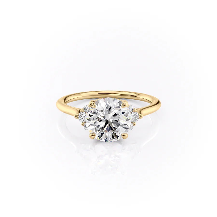 The Victoria. A Yellow Gold Three Stone, Side Stones Engagement Ring Set With A 2ct Round Lab Grown Diamond. White Background.